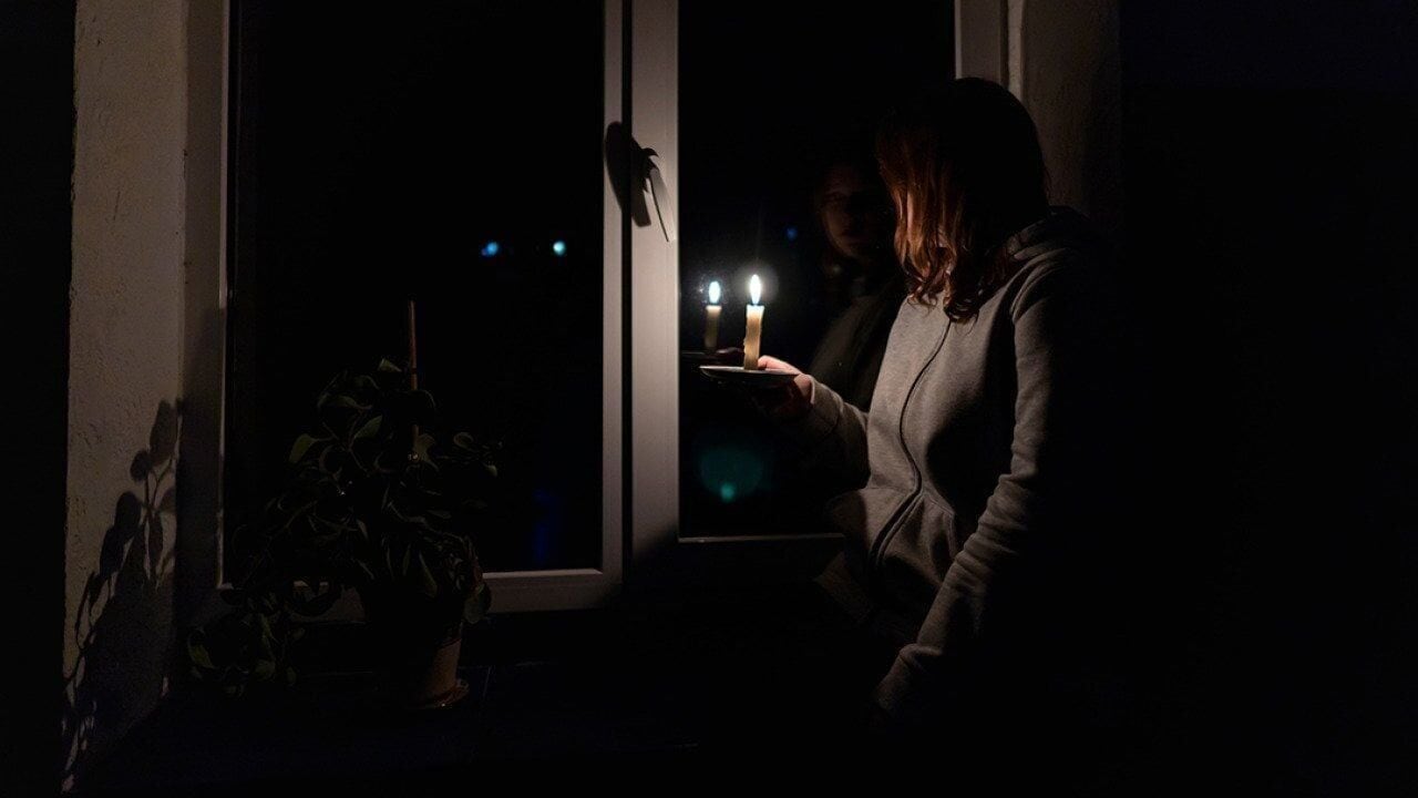 Woman with candle sits by window during a blackout.